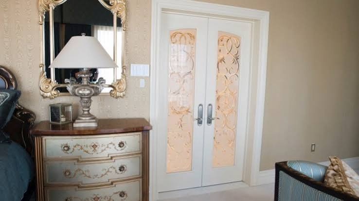 White double doors with tall carved glass panels beside a dresser and gilt mirror